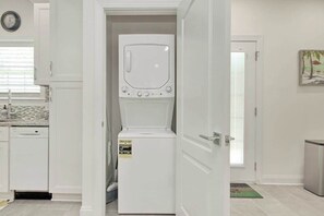 A compact kitchen with a dishwasher, a white refrigerator, and a door leading to another room. - Grace by the Sea Retreat (Atlantic Beach)