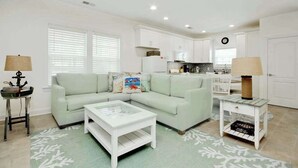 A modern living room with a light green sofa, a white coffee table, and a kitchen area with white cabinets and a black countertop. - Grace by the Sea Retreat (Atlantic Beach)