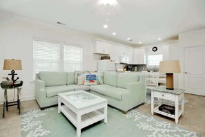 A modern living room with a light green sofa, a white coffee table, and a kitchen area with white cabinets and a black countertop. - Grace by the Sea Retreat (Atlantic Beach)