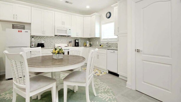 A modern kitchen with white cabinetry, a round dining table, and a clock on the wall. - Grace by the Sea Retreat (Atlantic Beach)