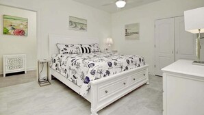 A bedroom with a bed, a nightstand, a lamp, a ceiling fan, and artwork on the walls. - Grace by the Sea Retreat (Atlantic Beach)