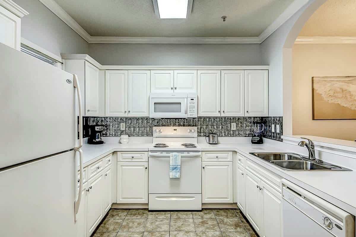Cocina compacta con gabinetes blancos, microondas, estufa y lavamanos.