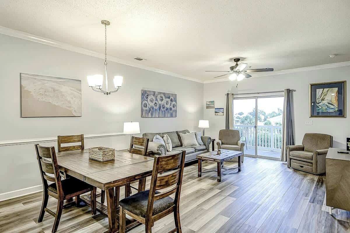 A spacious living area with a dining table, chairs, a sofa, and a balcony with a view.