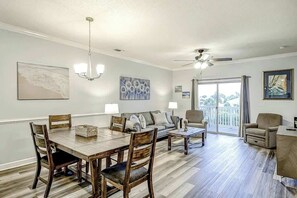 Uma sala de estar ampla com mesa de jantar, cadeiras, sofá e varanda com vista.