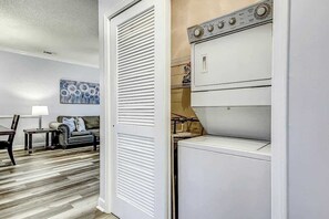 A laundry room with a washer and dryer, a sofa, a lamp, and a painting on the wall. - The Perfect Getaway at Wickham Dr (Myrtle Beach)