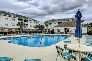 A swimming pool with lounge chairs and umbrellas, surrounded by multi-story buildings. - The Perfect Getaway at Wickham Dr (Myrtle Beach)