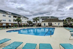 Ein Schwimmbecken mit Liegestühlen, ein Gebäude mit Balkon und eine Palme.