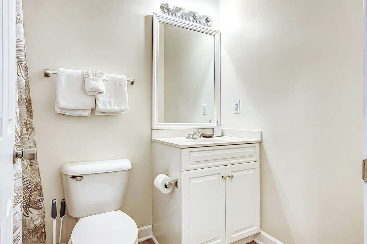 A bathroom with a toilet, a sink with a mirror above it, and two towels hanging on a towel rack.