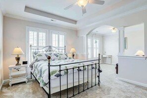 A bedroom with a bed, two bedside tables, lamps, a ceiling fan, and a large window. - Clearwater Bay Unit 1012 (North Myrtle Beach)