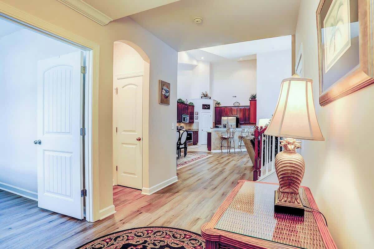 A hallway with a door, a lamp, and a rug leading to a kitchen area.