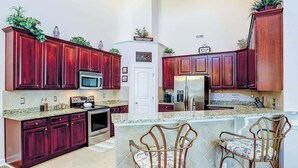 A kitchen with dark wood cabinets, a microwave, a refrigerator, and a double sink. - Clearwater Bay Unit 1012 (North Myrtle Beach)