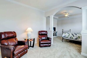 Ein Zimmer mit einem Bett, zwei Ledersesseln, einer Lampe und einem Deckenventilator.