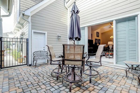 A covered patio with a table and chairs, a black metal gate, and a view into a house. - Clearwater Bay Unit 1012 (North Myrtle Beach)