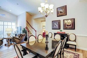 A dining area with a dark wooden table, multiple chairs, a chandelier, and framed artwork on the wall. - Clearwater Bay Unit 1012 (North Myrtle Beach)