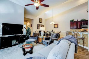Ein Wohnzimmer mit Fernseher, Sofa, Sesseln, einem Glastisch und Deckenventilator.