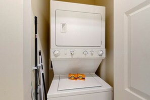 Eine weiße Waschmaschine mit Kisten mit Tide Waschmittel darauf, in einem kleinen Waschraum mit einer Tür rechts.