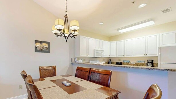 A dining area with a wooden table, chairs, a chandelier, and white cabinets in the background. - Paradise on the Course 303 (Myrtle Beach)