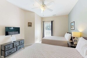 Ett hotellrum med två sängar, en platt-TV, en takfläkt och ett fönster med gardiner.