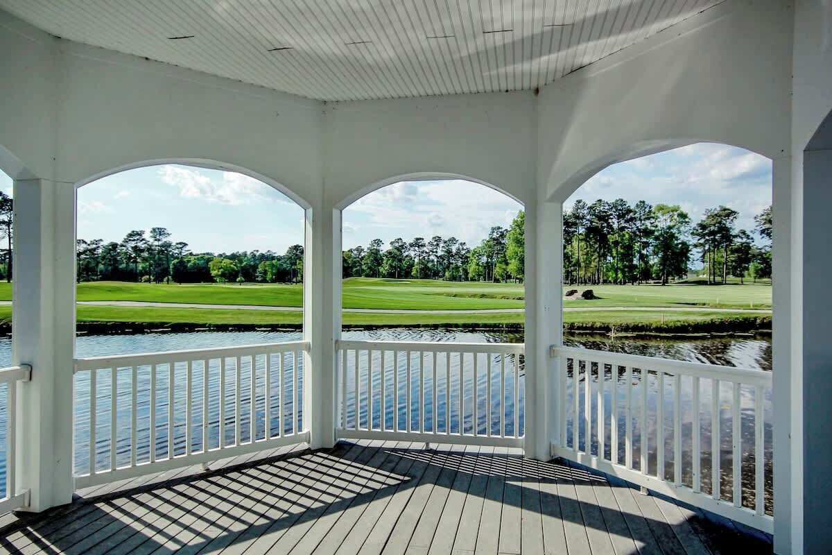 A covered outdoor area with a view of a golf course and a body of water.