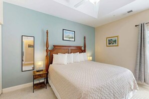 A hotel room with a large bed, a bedside table with a lamp, a ceiling fan, and two framed pictures on the walls. - Paradise on the Course 303 (Myrtle Beach)