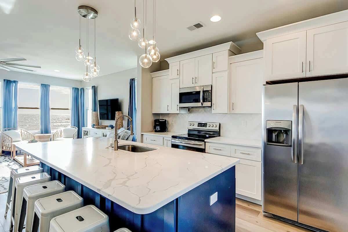 A modern kitchen with white cabinets, a large island with stools, stainless steel appliances, and pendant lighting.