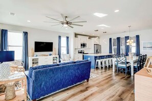 A modern living room with a blue sofa, a flat-screen TV, and a ceiling fan. - Blue Wave Beach Retreat (Murrells Inlet)
