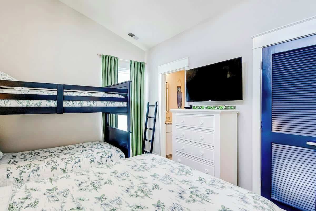 Ein Schlafzimmer mit Etagenbett, Flachbildfernseher, Kommode und blauer Tür.