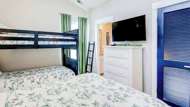 A bedroom with a bunk bed, a flat-screen TV, a dresser, and a blue door. - Blue Wave Beach Retreat (Murrells Inlet)