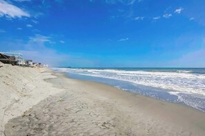 A beach with a clear sky, a sandy shore, and buildings along the coastline. - Blue Wave Beach Retreat (Murrells Inlet)