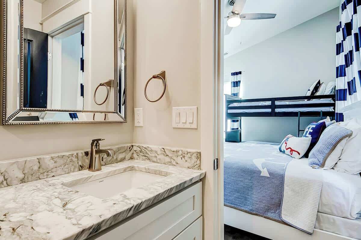 A hotel room with a marble bathroom vanity, a bed with a blue and white striped bedspread, and a ceiling fan.