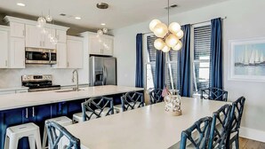 A modern kitchen with white cabinets, stainless steel appliances, and a central island with bar stools. - Blue Wave Beach Retreat (Murrells Inlet)