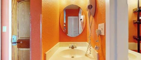 Une salle de bain avec un lavabo blanc, un miroir et un sèche-cheveux fixé au mur.