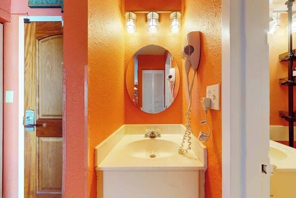 Een badkamer met een wit wastafel, een spiegel en een haardroger bevestigd aan de muur.