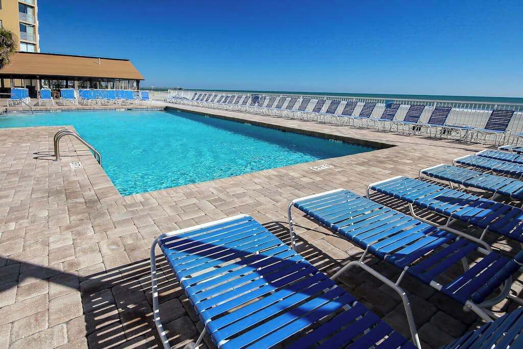 A pool area with blue lounge chairs and a clear view of the ocean.