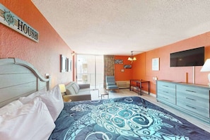 Ein Schlafzimmer mit einem Bett, einem Schreibtisch, einem Sessel, einem Fernseher und einem Fenster.