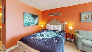 A bedroom with a bed, a nightstand, a chair, and a wall sign. - Sands Ocean Club 1101 Fruit Cakes (Myrtle Beach)
