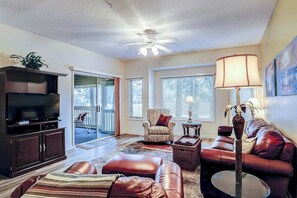 A living room with a television, leather sofa, armchair, and a ceiling fan. - Tidewater 4214 Condo (North Myrtle Beach)