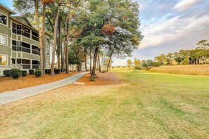 A two-story building with a covered walkway and a grassy area with trees. - Tidewater 4214 Condo (North Myrtle Beach)