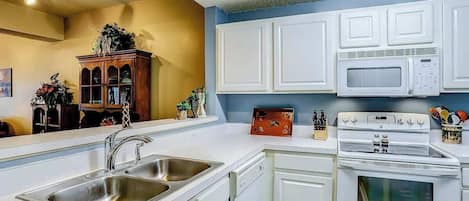 A modern kitchen with white cabinetry, a double sink, a microwave, and an oven.