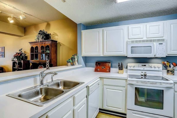 A modern kitchen with white cabinetry, a double sink, a microwave, and an oven. - Tidewater 4214 Condo (North Myrtle Beach)