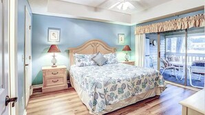 Ein Schlafzimmer mit einem Bett, Nachttischen, einem Deckenventilator und Blick durch ein Fenster.