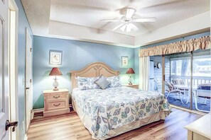 A bedroom with a bed, bedside tables, a ceiling fan, and a view through a window. - Tidewater 4214 Condo (North Myrtle Beach)