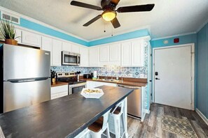 A modern kitchen with white cabinets, a stainless steel refrigerator, a microwave, and a ceiling fan. - Cherry Grove Pelican's Watch (North Myrtle Beach)