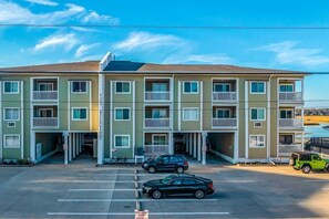 A multi-story apartment building with balconies, a parking lot, and a clear sky. - Cherry Grove Pelican's Watch (North Myrtle Beach)