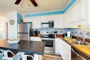 A modern kitchen with white cabinets, a stainless steel refrigerator, a microwave, an oven, and a sink. - Cherry Grove Pelican's Watch (North Myrtle Beach)