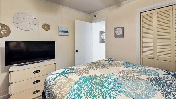 Ein Schlafzimmer mit einem Bett, einem Fernseher auf einer Kommode, einer Tür und einer Uhr an der Wand.