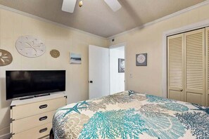 A bedroom with a bed, a television on a dresser, a door, and a clock on the wall. - Cherry Grove Pelican's Watch (North Myrtle Beach)