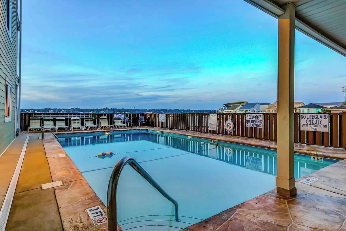 En indendørs swimmingpool med udsigt til byens skyline, omgivet af en træterrasse og et overdækket område.