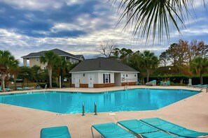 Une piscine avec des chaises longues, un petit bâtiment et des palmiers.