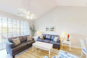Ein Wohnzimmer mit einer Sofagarnitur, einem Couchtisch, einem Bild an der Wand und einem Deckenventilator.